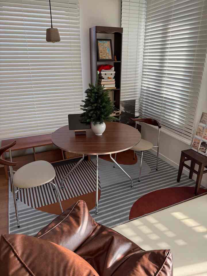 ブラウンとホワイトの色調のダイニング、丸いダイニングテーブルと椅子、ラグが配置された温かみのあるモダンな空間