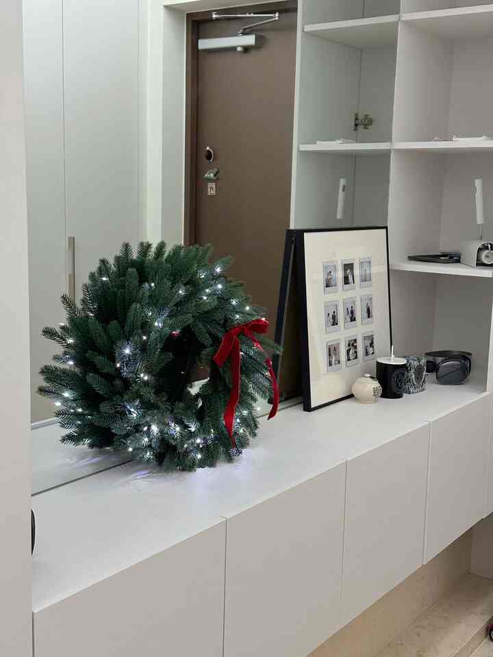 白を基調とした清潔感のある玄関、クリスマスリースと額縁が配置されたミニマルなインテリア