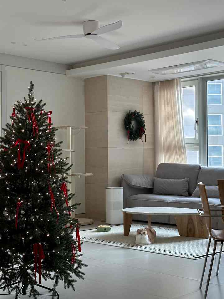 ナチュラルな色調のリビングにクリスマスツリーとグレーのソファ、丸いコーヒーテーブルが配置された雰囲気のあるインテリア