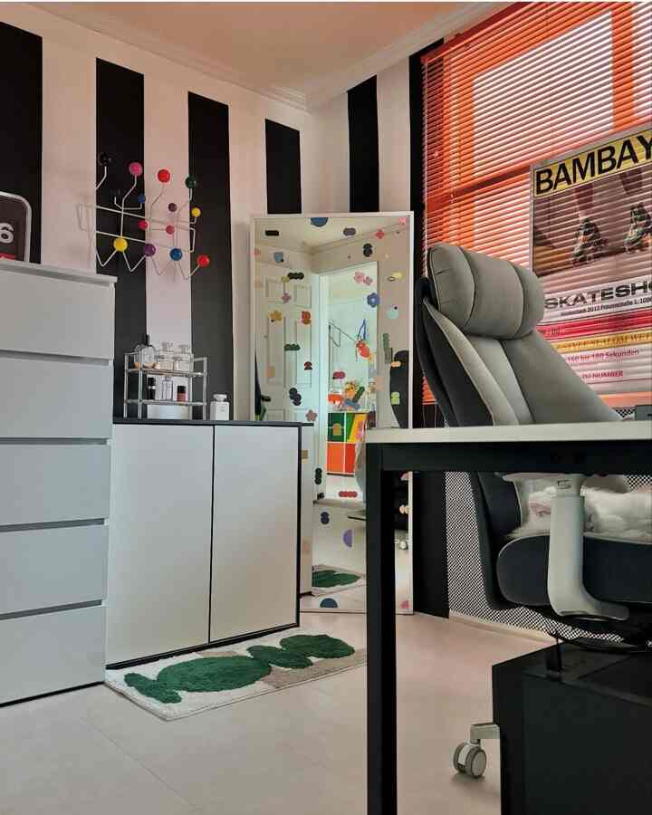 白と黒のストライプ壁、オレンジのブラインドがあるシンプルモダンなホームオフィス、机とオフィスチェア、猫がいる空間