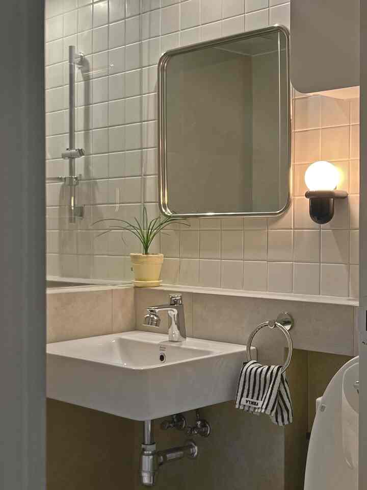 白とベージュのトーンのモダンなトイレ、クロームの蛇口と丸い壁照明が配置された雰囲気のある空間