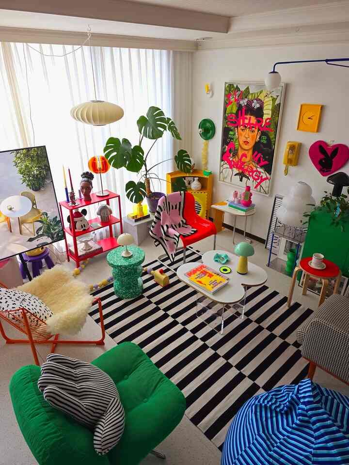Bright living room with white walls, featuring a black striped rug, green armchair, and red chair arranged in a vibrant mid-century modern style