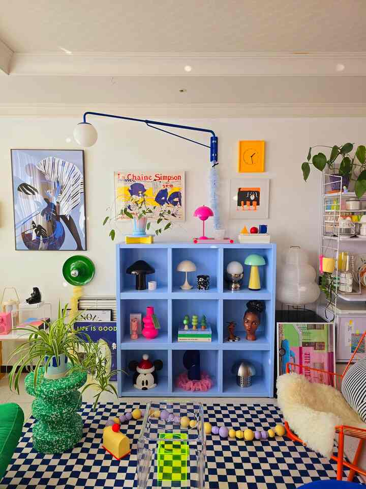 Pastel blue-toned living room featuring colorful objects, artworks, and plants arranged harmoniously with a bright, lively atmosphere