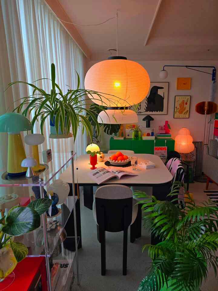 Ivory-toned living and dining room featuring a white dining table with pendant lights, green cabinet, and lush plants creating a cozy atmosphere