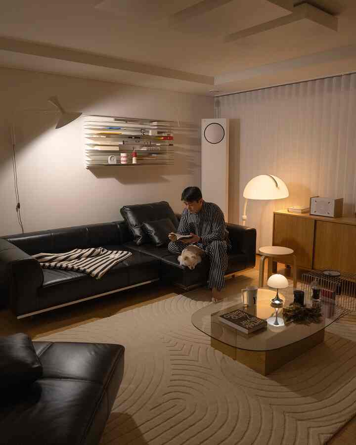 黒革のソファとベージュのラグが特徴的なナチュラルモダンなリビング。男性がソファで読書をし、犬がそばにいる。