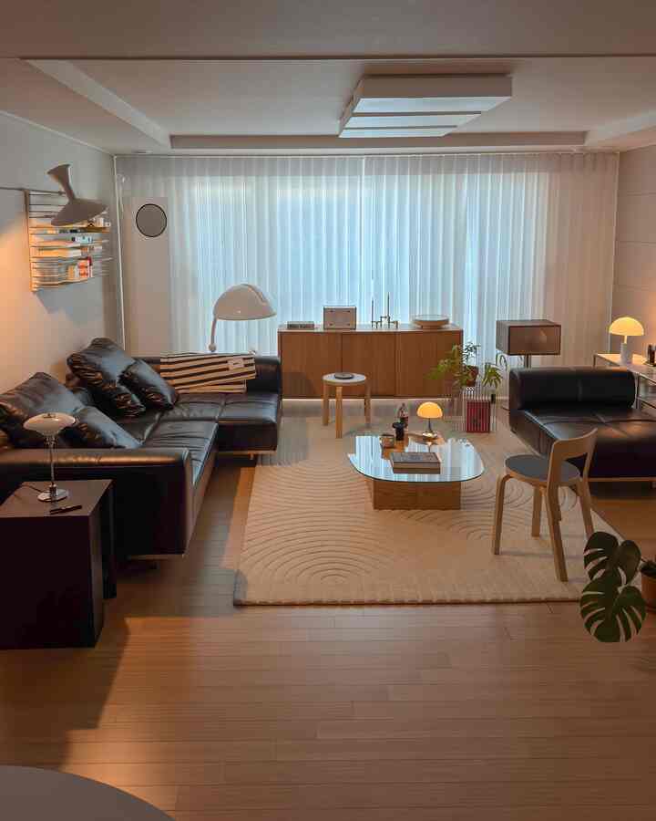 木目調の床と黒のレザーソファが配置されたモダンなリビング、クリーム色のラグと多彩な照明が調和する雰囲気のある空間