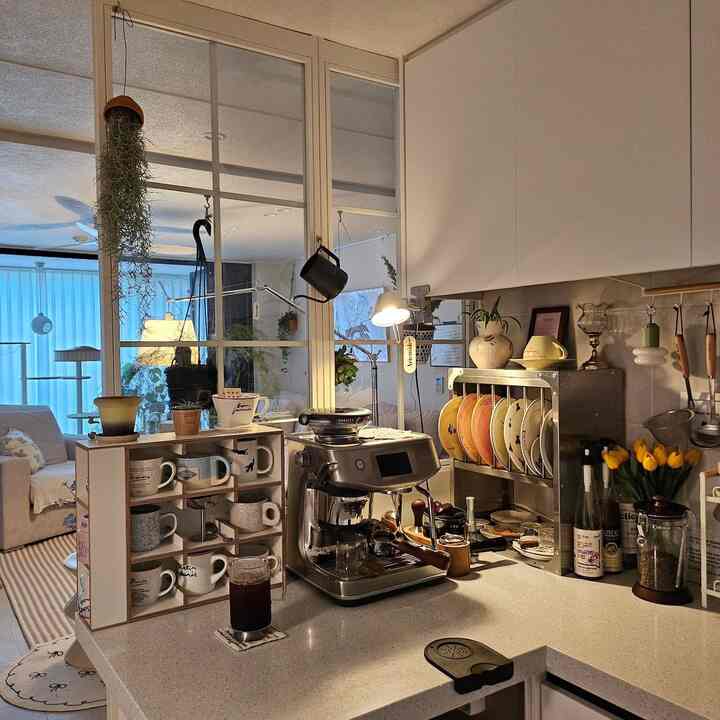 温かみのある色調のキッチンスペース、コーヒーマシンとカップ棚が配置されたモダンで雰囲気のあるおうちカフェインテリア