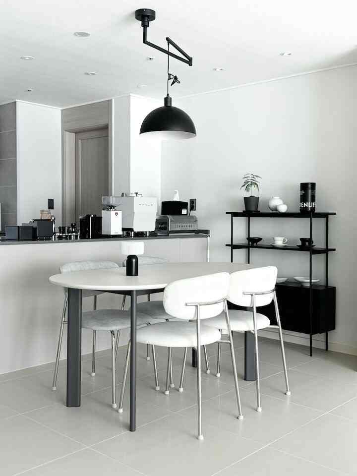 モノトーンのキッチンスペース、シンプルモダンなダイニングテーブルと椅子が配置され、黒のペンダントライトが調和する清潔感のあるインテリア