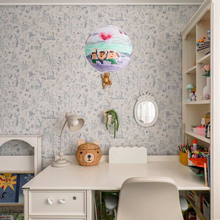 青い柄の壁紙がある子供部屋、白い机と本棚、子どものアイテムで落ち着いた勉強空間
