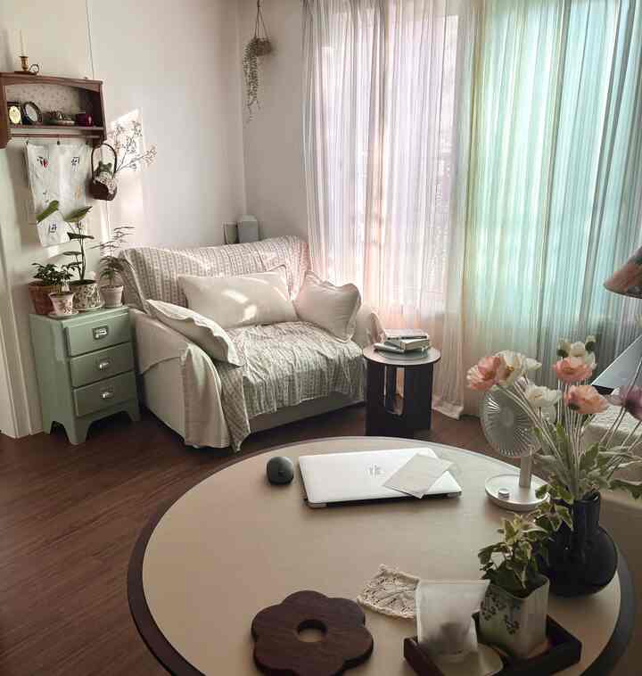 アイボリーとホワイトのトーンの小さなリビング、1人掛けソファと丸テーブル、植物とヴィンテージのチェストが配置された雰囲気のあるインテリア