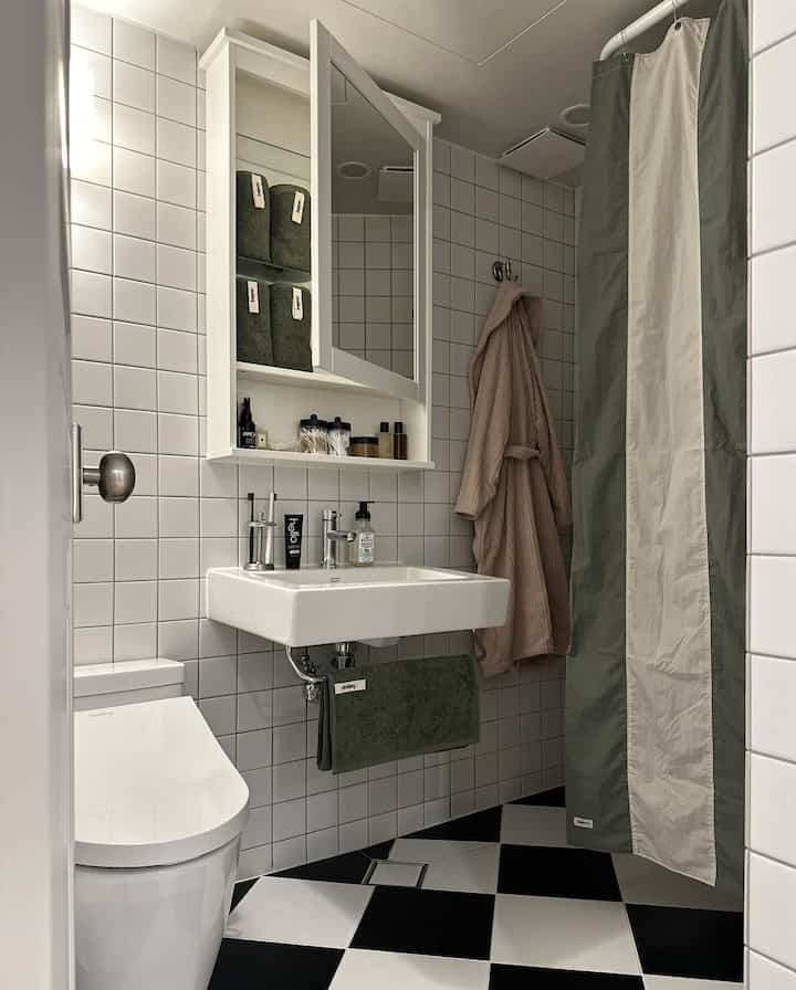 白と黒のタイルが調和したバスルームで、洗面台、タオル掛け、クラシックな鏡が配置された清潔感のあるインテリア