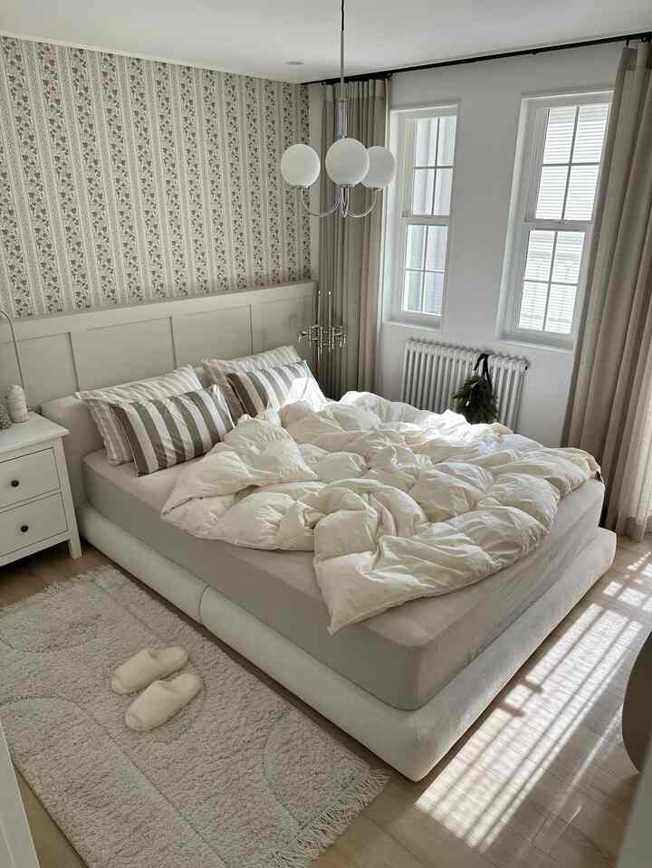 白とベージュの色調の北欧風寝室、シャンデリアとラジエーターが配置された居心地の良い空間