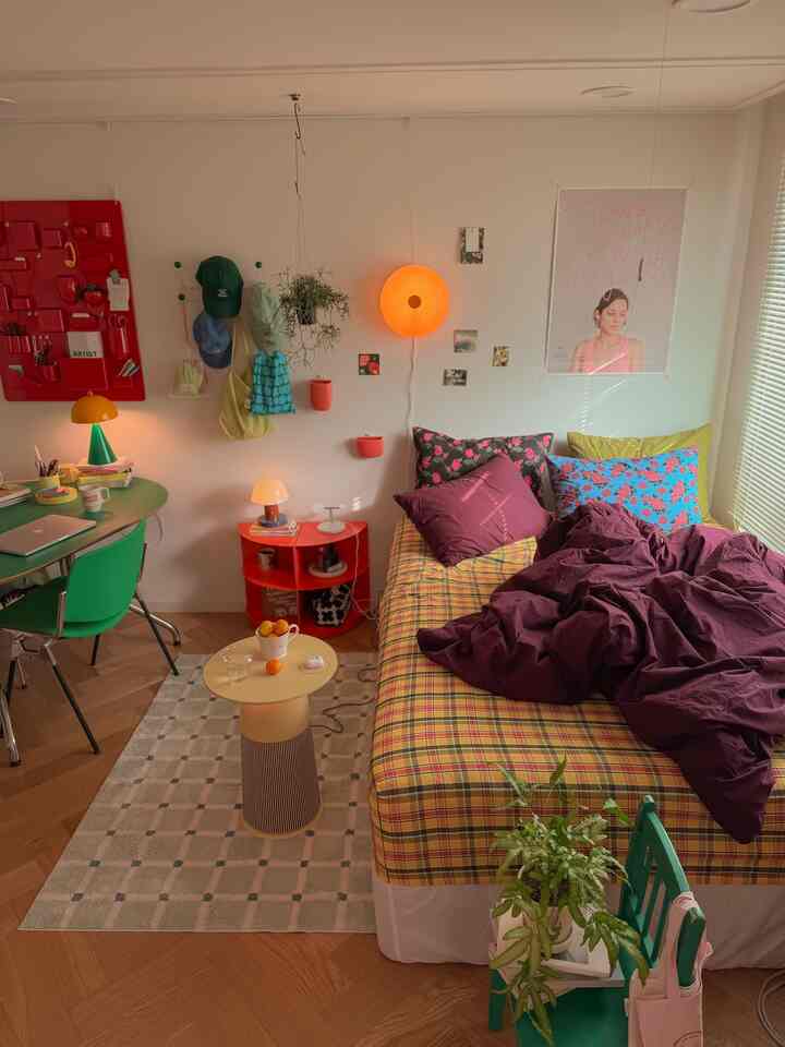 黄色のチェック柄ベッドとオレンジのムードライト、緑のデスクと椅子が配置された居心地の良いボヘミアンスタイルの寝室