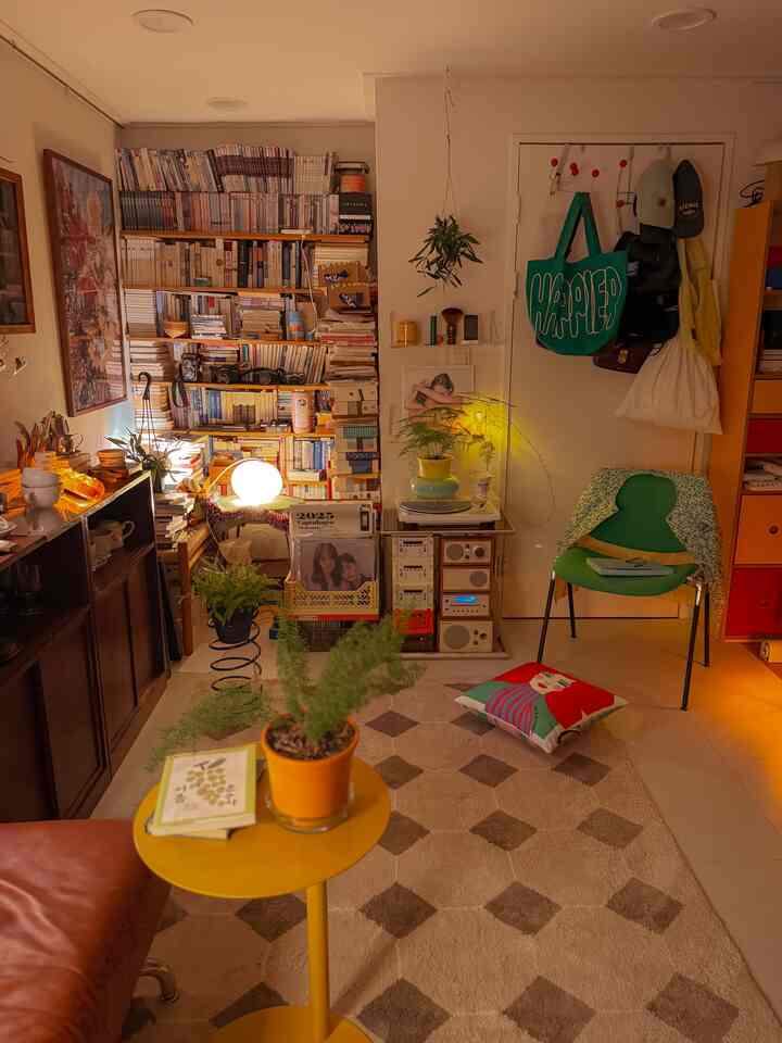 Cozy living room in warm yellow and green tones featuring a bookshelf and plants with retro ambiance