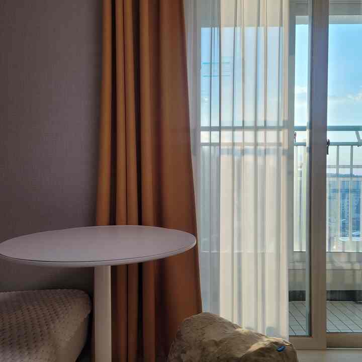 ブラウンとホワイトの色調のリビング、2人掛けソファと丸テーブル、シフォンカーテンとバルコニーが調和した落ち着いたインテリア