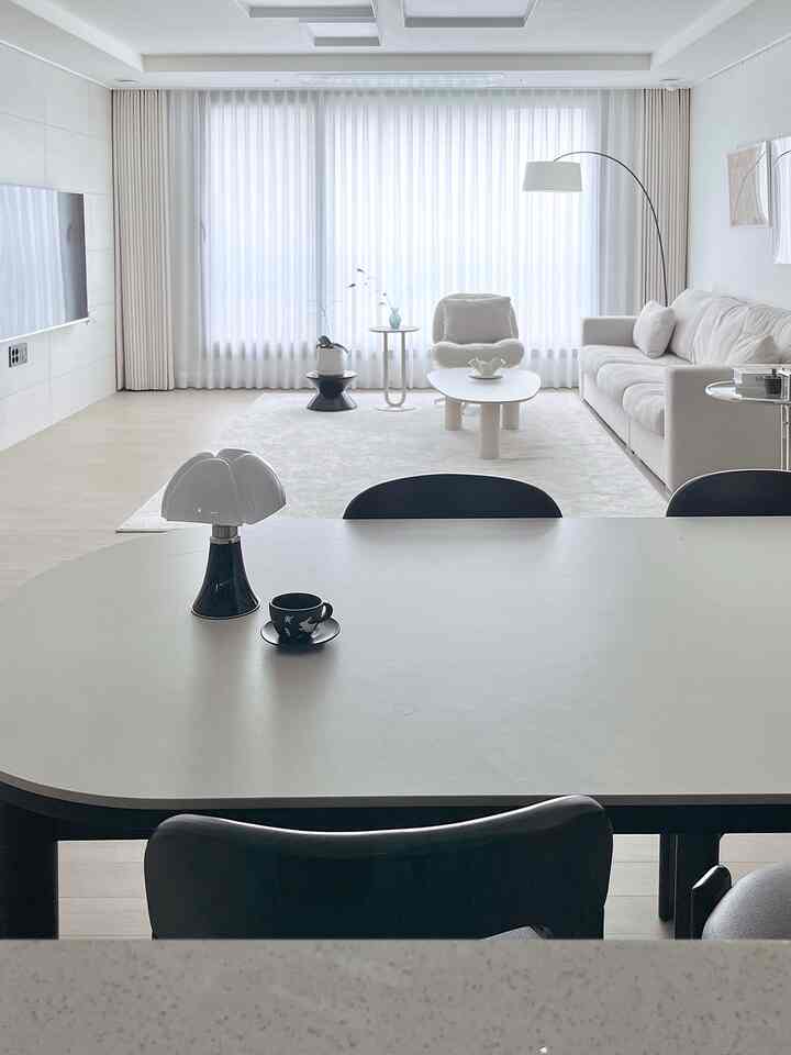 柔らかなホワイトとベージュの色調のリビング。白いソファ、カーテン、シンプルなテーブルとフロアランプが配置されたモダンな空間