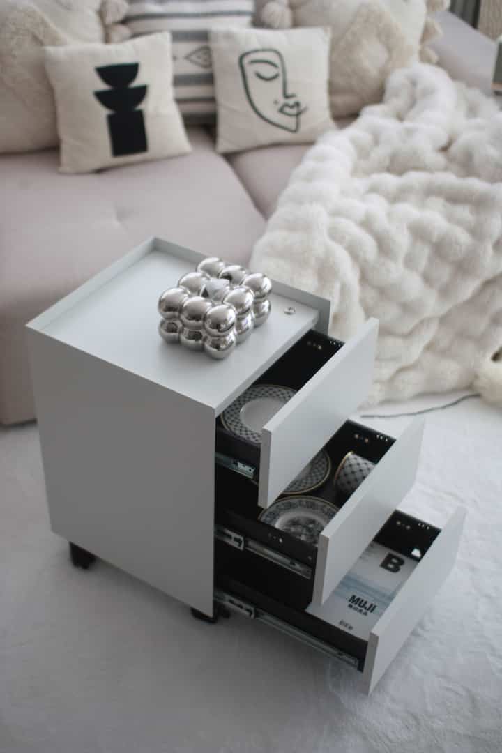 ベージュと白の色調のリビング、引き出しが開いたキャビネットとクッション、暖かみのあるブランケットが配置された雰囲気のある空間