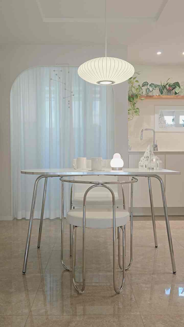 白とシルバーのトーンが基調のモダンなキッチン兼ダイニング空間、ペンダントライトとダイニングチェアが配置された洗練されたインテリア