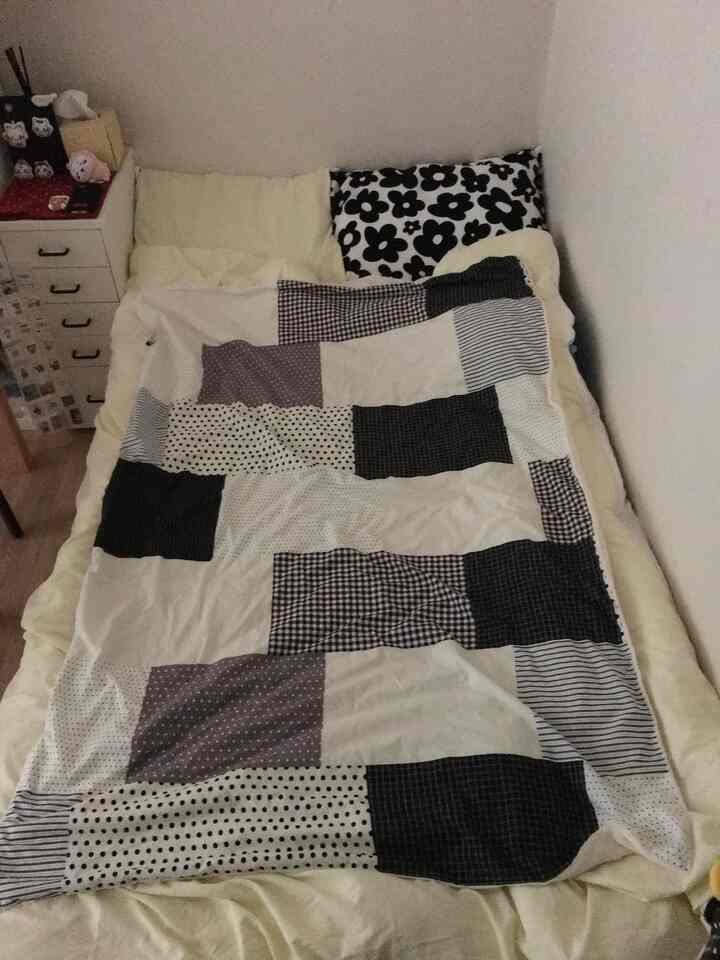 白を基調とした寝室に、モノトーンのパッチワークブランケットと枕が配置された雰囲気のある空間