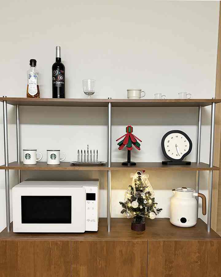 白い壁とブラウンの木製棚が特徴のホームカフェ空間、電子レンジとクリスマスツリーの装飾が温かみのある雰囲気を演出