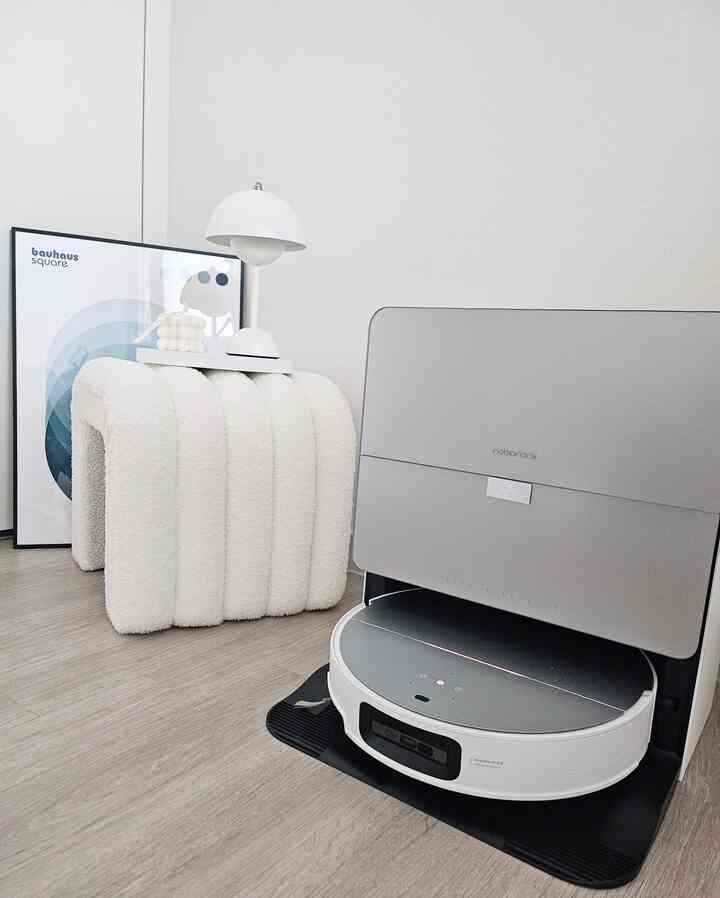 白を基調とした小さな部屋、モダンなロボット掃除機と独特な曲線のデスク、照明が配置された雰囲気のあるインテリア