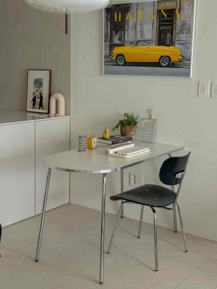 ホワイトとクローム調の調和が取れたコンパクトなホームオフィス空間、楕円形のダイニングテーブルと黒いチェアが配置された清潔感のあるインテリア