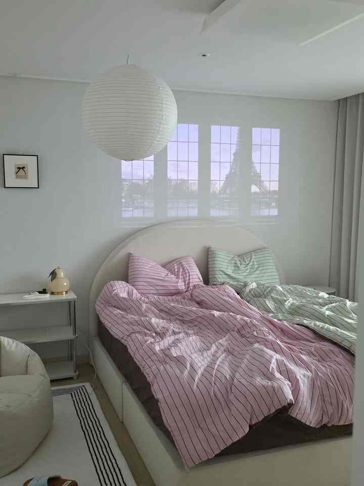 White and pink toned newlywed bedroom featuring a bed, nightstands, and a bean bag in a clean hotel-like setting