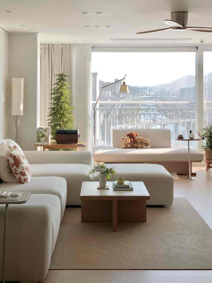 白とベージュのトーンのリビング、窓辺にデイベッドとソファ、植物が配置された自然でモダンな雰囲気のインテリア