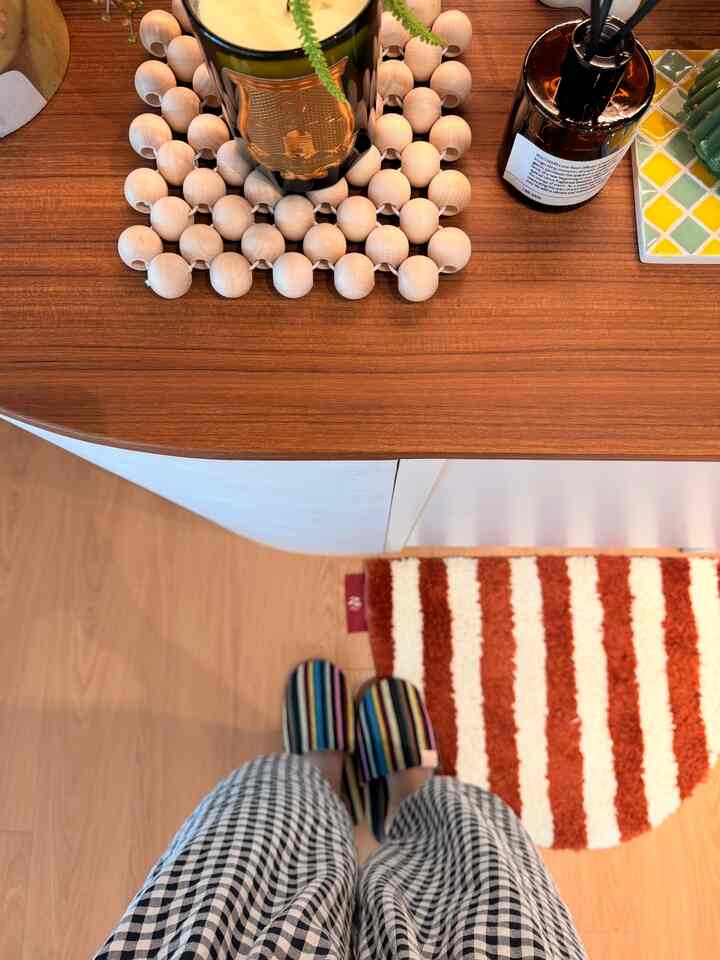 木目調のテーブルに丸いウッドコースターとキャンドル、赤と白のストライプのバスマットとカラフルなスリッパが配置された落ち着いた玄関スペース