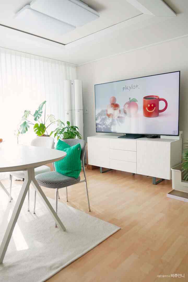 明るいホワイトとベージュの色調のリビング兼ダイニングルーム、白いテレビ台とダイニングテーブル、植物が配された自然な雰囲気のインテリア