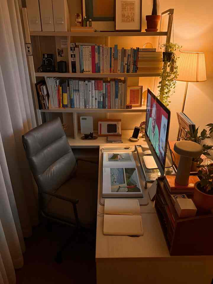 ナチュラルカラーとチャコール色調のホームオフィス、机、マットなレザーの椅子、本棚、暖かい照明がある雰囲気のある書斎