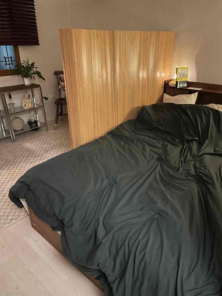 A cozy bedroom with wood tone and dark gray hues, featuring a central room divider
