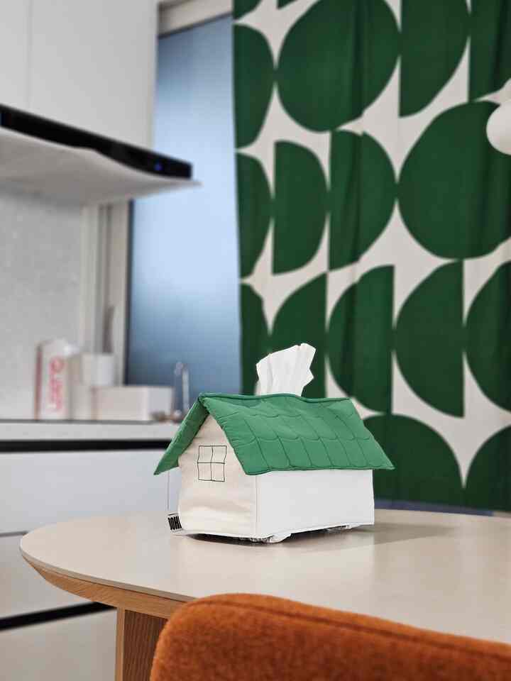 ナチュラルカラーのキッチンとダイニングスペース、家の形のティッシュケースとオレンジ色のクッションが置かれた雰囲気のあるインテリア