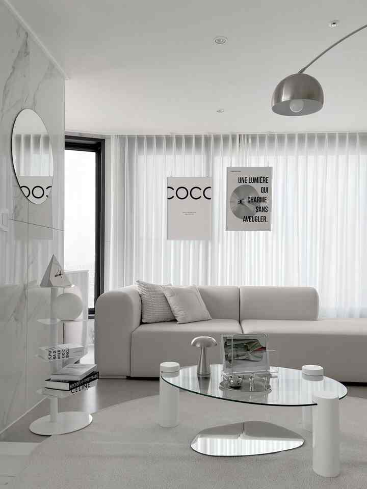 白とシルバーの色調のリビング、モジュールソファとガラスのコーヒーテーブル、額縁やメタル照明が配置されたシンプルでモダンなインテリア