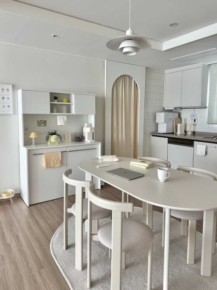 ホワイトと木目調の4人用キッチン、丸いラグとアーチ型の間仕切りが配置された落ち着いたミニマルなおうちカフェ風の空間