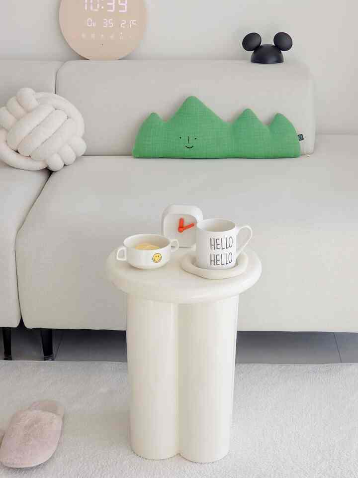 明るいホワイトトーンのリビング、シンプルなソファとグリーンクッション、小さな白いナイトテーブルが配置された落ち着いた空間