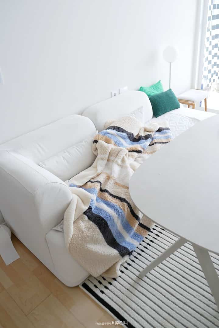 明るいホワイトトーンのリビング、白いソファにストライプ柄のスローとラグが配置されたシンプルで清潔感のあるインテリア