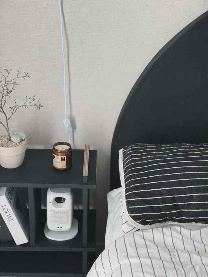 モノトーンの黒と白の寝室、黒いカーブしたヘッドボードとストライプの枕カバー、黒い棚の上に造花とキャンドルが置かれた雰囲気のあるインテリア