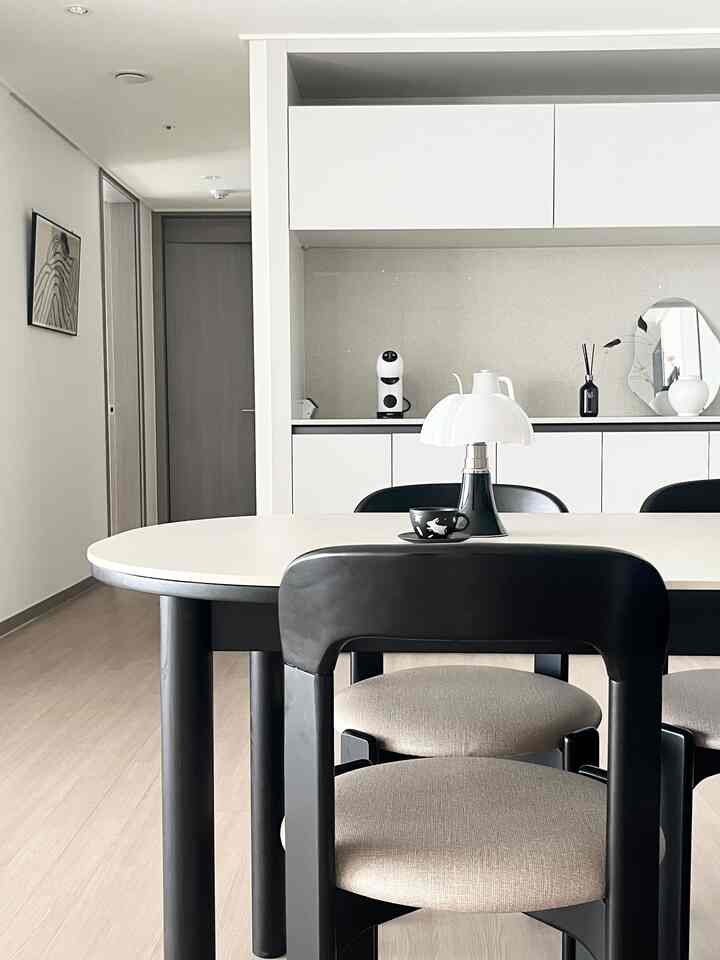 モノトーンのキッチンとダイニングスペース、白い吊り戸棚と黒いダイニングチェアが配置されたシンプルなインテリア