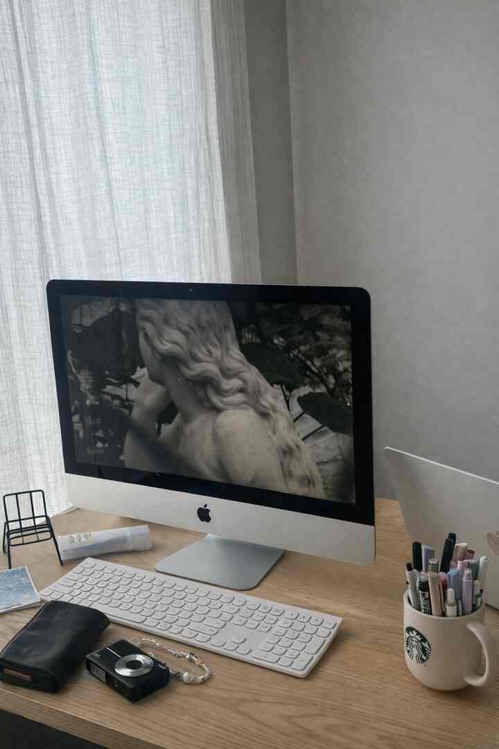 Wood tone home office featuring a 2008 iMac with white keyboard on a neat desk, complemented by soft white curtains creating a cozy atmosphere