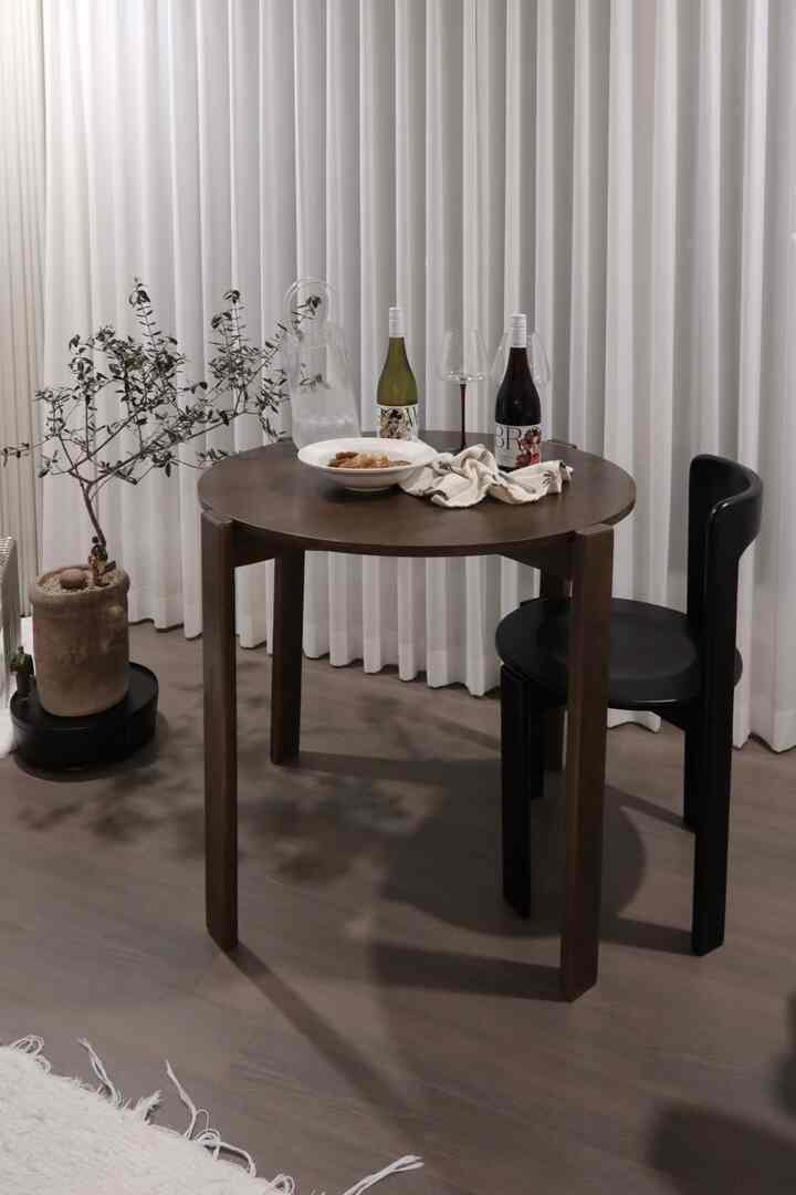 ナチュラルなブラウン色調のリビングダイニングテーブルと黒のダイニングチェア、白いカーテンを背景にしたミニマルな雰囲気の空間