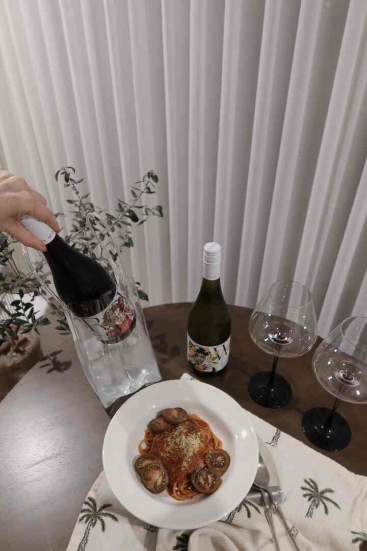 Home cafe space featuring brown wooden dining table with wine glasses, wine bottles, and a pasta plate against white curtain background