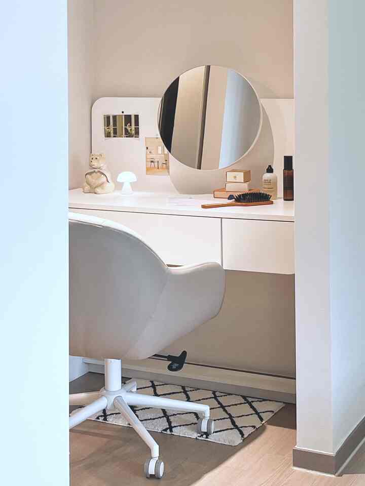 アイボリーとベージュのトーンのウォークインクローゼットの化粧台スペース、丸い鏡とミニLEDランプが配置されたミニマルなインテリア