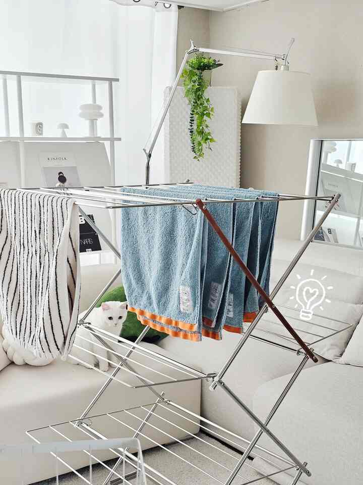 ナチュラルトーンのリビング、シルバーのステンレス製乾燥ラックとホワイトソファが配置された温かみのある清潔なインテリア