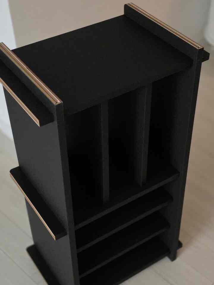 黒い紙製のミニマルな本棚が明るい床の上に置かれ、小さな空間に適した家具