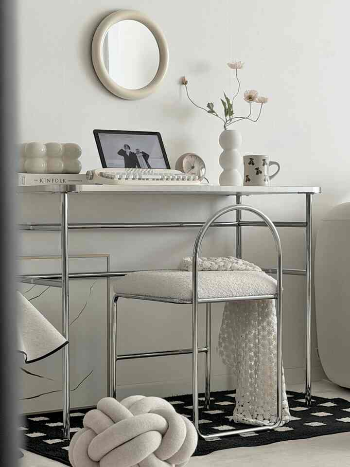 White and silver toned home office featuring a simple desk and round mirror with minimal decor elements
