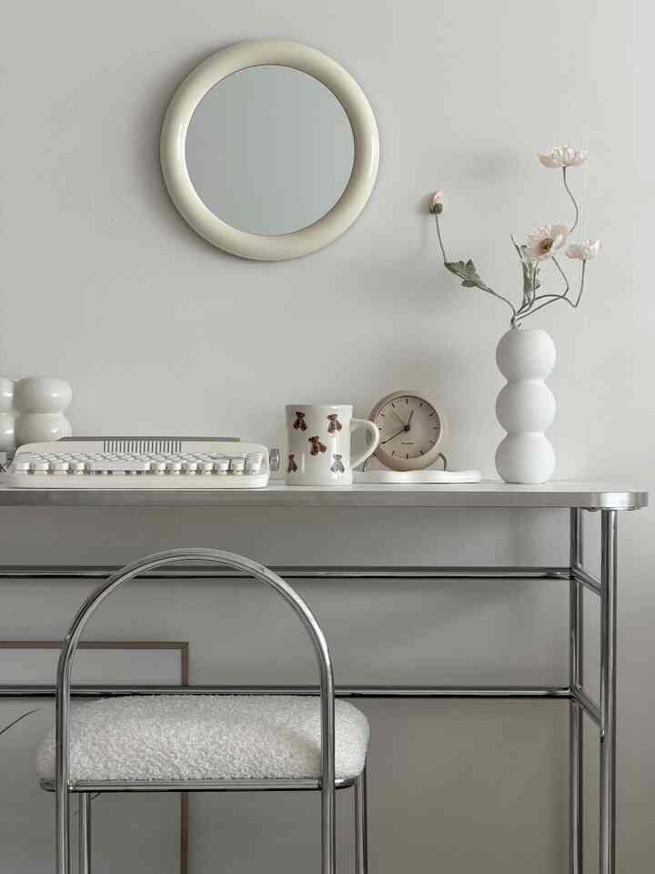 White-toned vanity space with a round mirror and vase, featuring a minimalistic interior design