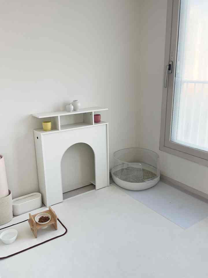 明るいホワイトトーンの暖炉コンソールと猫トイレが配置された清潔感あるペットスペース