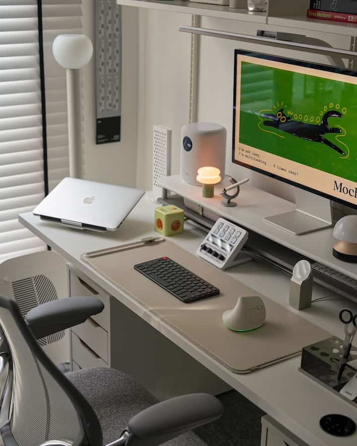 白とベージュのトーンのホームオフィス、スリムなデスクとモニタースタンド、スマートデバイスが配置された印象的なインテリア