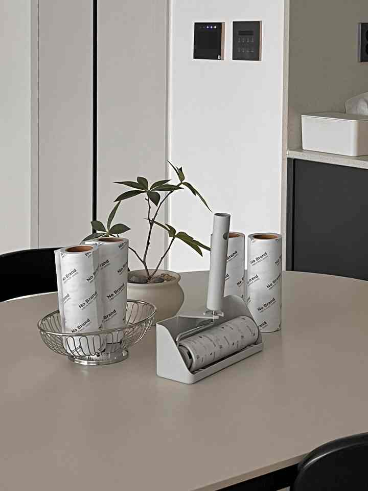 ホワイトとベージュのトーンのキッチンテーブルに造花鉢とテープクリーナー、ローラータイプのホコリ取りが配置された清潔感のあるインテリア